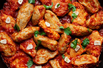 Close-up macro texture view of poultry and dumplings stew in tomato sauce with garlic and coriander garnish.