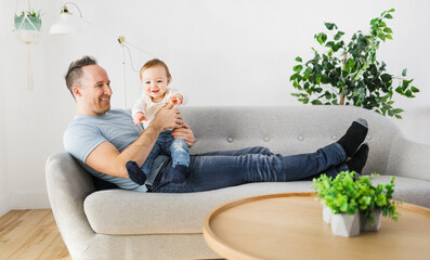 father playing with cute baby daughter on the sofa