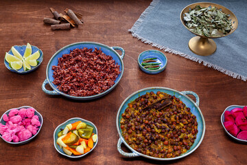 Set of plates and bowls on wooden table. Black chickpea (Kala chana) curry and red rice, vegetable pickles. Vegan meal.