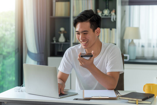Young Asian man enjoys talking on the phone. Look at the laptop screen at home.