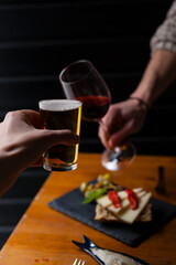 Two friends making a toast with beer and wine on a tapas bar background with negative space.
