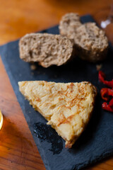 Spanish omelette slice served on a chalk board with organic bread and peppers. Typical tapas food from Spain.