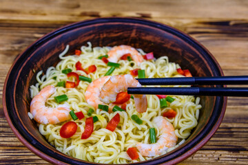 Instant noodle with shrimps, red pepper and green onion in a ceramic bowl. Japanese food. Chopsticks with shrimp