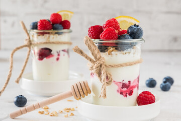 Yogurt with berries, cereals and honey in a glass on white background