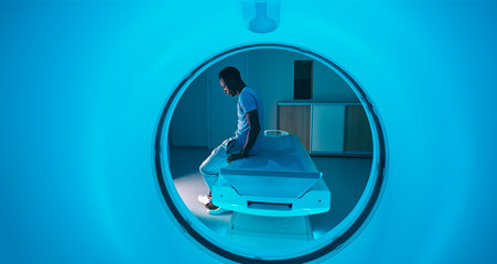 Black patient lying down on CT machine table near doctor