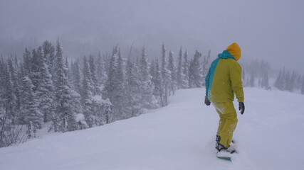 Fototapeta na wymiar Snowboarder find fresh powder through the trees during snowfall in mountains. Slow motion