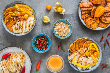 Buddha bowls with spicy chicken, rice, bell pepper, sweet potato and minced peanuts, trend and healthy food, top view on gray background