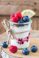 Yogurt with berries and cereals in a glass on a rustic wooden table, vertical