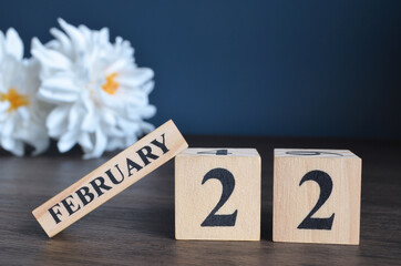 February 22, Date cover design with calendar cube and white Paeonia flower on wooden table and blue...