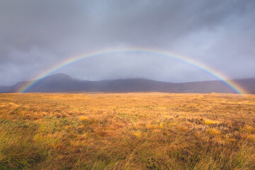 A full colourful rainbow in a moody countryside landscape near Glencoe in the Scottish Highlands, Scotland.