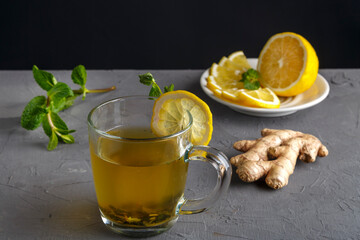 vitamin ginger drink with honey mint and lemon in a glass cup near the ingredients on a concrete background.