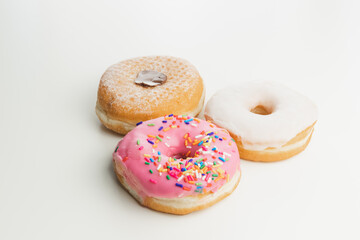 Three fresh, colourful ring doughnuts isolated on a plain white surface and background.
