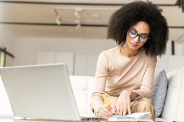Smart young African American student or businesswoman sitting on the couch with laptop, studying...