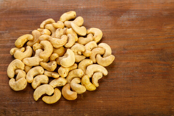Cashew nuts are sprinkled on a dark wooden table.