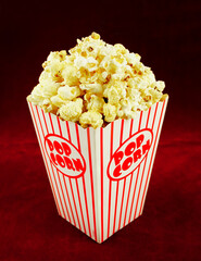 Delicious popcorn in a red striped paper cup on a red background.