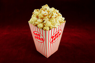 Delicious popcorn in a red striped paper cup on a red background.