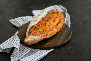 A whole loaf of homemade wheat bread on a wooden board against a dark concrete background.