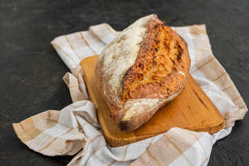 A whole loaf of homemade wheat bread on a wooden board against a dark concrete background.