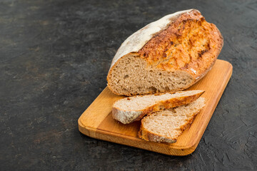 Sliced loaf of wheat homemade bread on a wooden board against a dark concrete background.