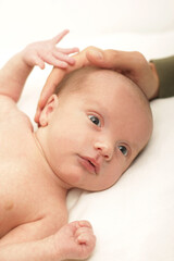 baby lying on its back on a white background with its father's hand on its hea