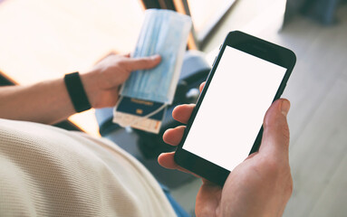 The man holding the mobile phone with empty space as a mockup for digital vaccination certificate in one hand and passport, mask and ticket in another one