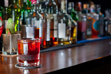 Yellow cocktail on bar counter. Whiskey, rum or brandy on the background of bottles with alcohol. Glass with booze on a wooden board.