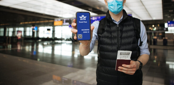 IATA Travel Pass Initiative. Phone in airport and airplane in the background. Passport and flight tickets. Hand holding mobile COVID-19 app for vaccination
