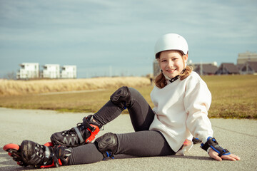 Portrait of pretty little teenager child girl sitting in white helmet, inline skates and safety...
