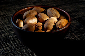 Pecan in a clay bowl on a shabby wooden board. Nuts in shell on an old black table. Contrasting dramatic light as an artistic effect.