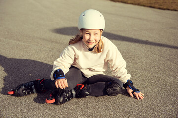 Portrait of pretty little teenager child girl sitting in white helmet, inline skates and safety...