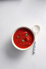 Tomato soup in a white bowl on white background. Top view. Copy space