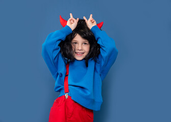 Spoiled child, naughty girl, kids whims. Beautiful little girl in wig with red imp horns showing...