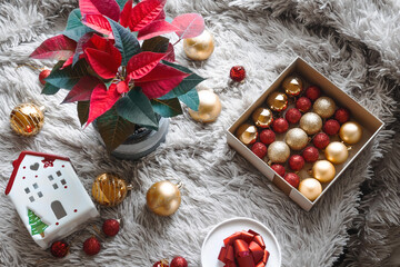 Happy New Year and Merry Christmas. A box with Christmas balls on a light background. Christmas poinsettia in the background.