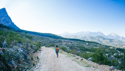 A woman with a backpack is walking along a mountain road.