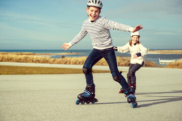 Happy siblings teenager boy and girl having fun during inline skating at sunny day at Baltic sea promenade