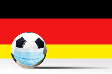 Obraz premium Soccer ball in a medical mask against the background of the flag of germany. Corona protection against viruses bacteria stop. Cancellation of sporting events. Copy space