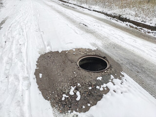 Dangerously open hatch on the road without warning fences. Danger on the road. Snowy road with an open hatch
