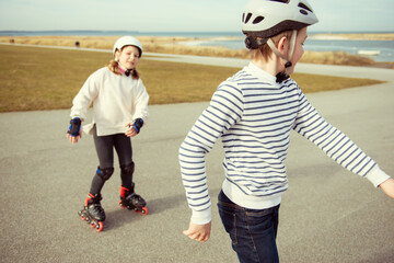 Happy siblings teenager boy and girl having fun during inline skating at sunny day at Baltic sea...