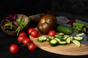 Ingredients for making salad on rustic black board background. Vegetable salad in bowl, tomato, cucumber, tomatoes kumato. Healthy, clean eating concept. Vegan or gluten free diet