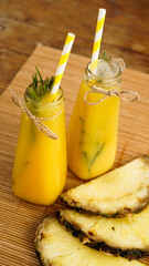 Fresh made Pineapple Juice with Ice in a small glass bottle on wooden background. Homemade drink.