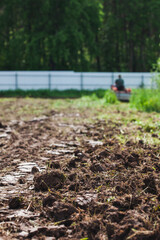 A man on a track cultivator digs a private plot. Focus on the foreground on clods of earth