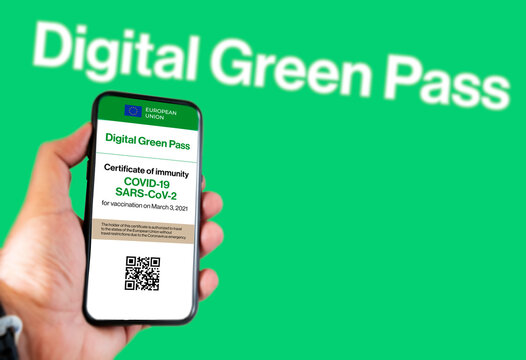 The digital green pass of the european union with the QR code on the screen of a mobile held by a hand with a blurred green background