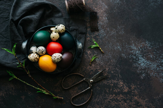 Vintage iron tray full of colorful Easter eggs with hay and spring branch on a dark rustic background. Top view with copy space.