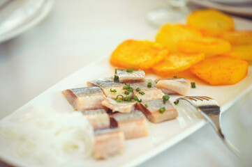 Delicious pieces of Icelandic herring with onions on a white plate. Raw salted herring on wooden background. Marinated herring fillet with grilled potatoes