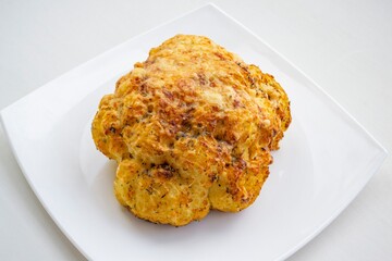 Grilled cauliflower (with cheese and spices) on a white plate, in bright daylight