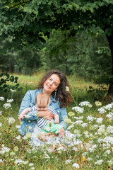 Fototapeta na wymiar mom and baby are sitting in a park under a tree among the flowers and smiling.Flower field, picnic outdoors