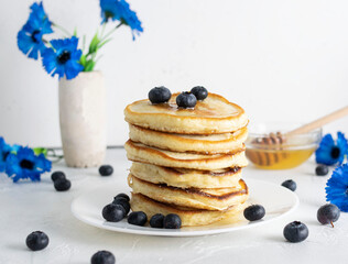 Pancakes on kefir lie on a white plate with blueberries