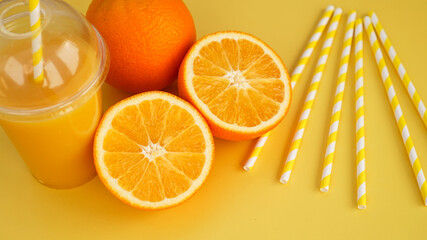 Orange juice in fast food closed cup with tube on yellow background. Sliced orange and yellow paper straws for a drink