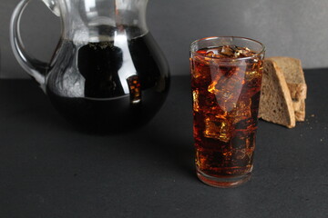Dark bread kvass poured into a glass with solder and stands in a jug on a gray black background with a place for text and copyspace
