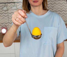 Young woman holding colored yellow egg in a ladle. Preparing for The Easter.